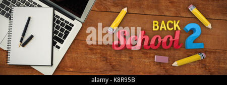 Back to school message against overhead view of laptop with pen and book on table Stock Photo