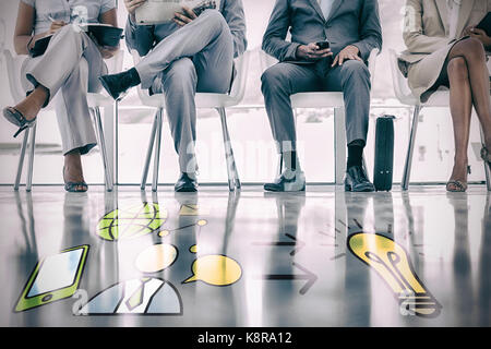 Various icons pointing towards light bulb against low section of business people waiting Stock Photo