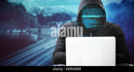 Hacker wearing black hood while using laptop on table against high angle view of crowded buildings in city Stock Photo