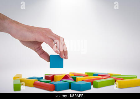 Cropped hand arranging colorful blocks against grey background Stock Photo