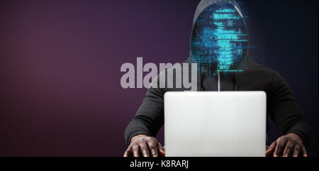 Male hacker with laptop on table  against pink and purple colors background Stock Photo