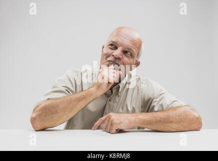 Pleased man sitting thinking with a smile of anticipation on his face as he sits at a table over white looking up onto the air Stock Photo
