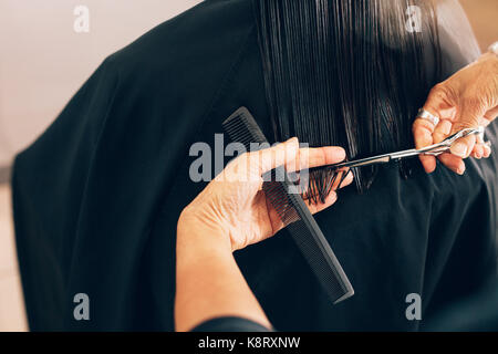 Close up of hair stylist cutting the hair to a straight level. Hairdresser using comb and scissors for a hair cut. Stock Photo