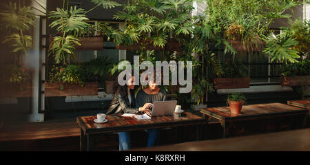 Two women sitting with a laptop and notepads at a table. business colleagues working while having coffee. Stock Photo
