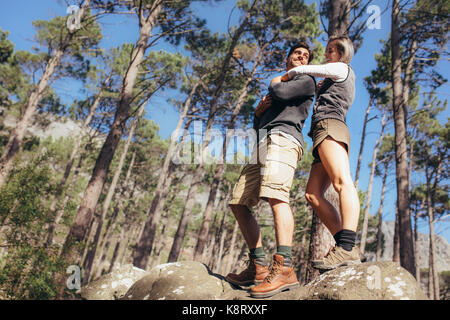 Happy hiking couple having fun while trekking in forest. Woman holding man with arms around his shoulders standing on rocks with trees in the backgrou Stock Photo