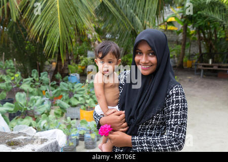 Maldives people - a young Maldives asian muslim woman carrying a child, Rasdhoo village, the Maldives, Asia Stock Photo