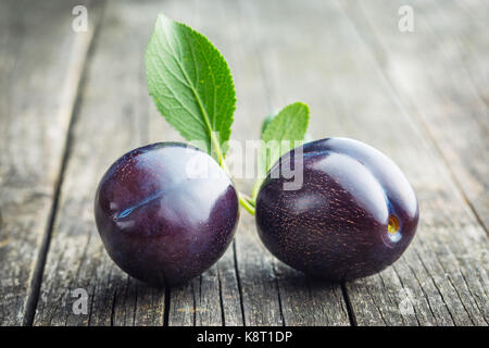Two fresh plums on old wooden table. Blue plums with leaves. Stock Photo
