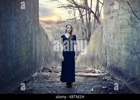 beautiful lonely girl  in long dress near gloomy tunnel on sunset Stock Photo