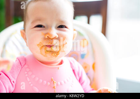 Adorable baby girl making a mess while feeding herself Stock Photo