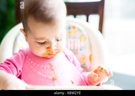 Adorable baby girl making a mess while feeding herself Stock Photo