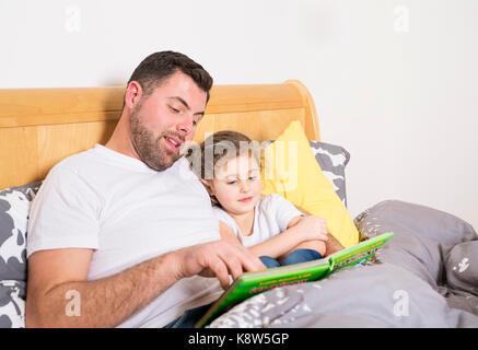 Happy father reading a story to his daughter in a bedroom Stock Photo