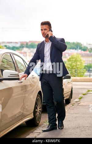 A handsome young businessman walking to his car on the street while talking on his phone Stock Photo