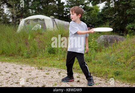 brown haired boy throws a white frisbee at a campground Stock Photo