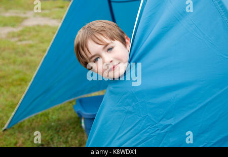 cute brown haired child plays hide and seek inside a blue tent while camping Stock Photo