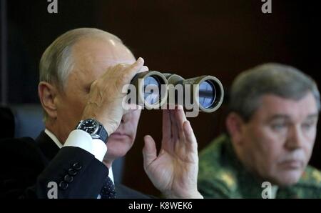 Russian President Vladimir Putin looks through binoculars as Russian Armed Forces General Valery Gerasimov, right, looks on during military exercise at the Luzhsky Range training ground September 18, 2017 outside St. Petersburg, Russia. Stock Photo