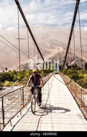 Man riding a bike on a footbridge and Cerro Toro Mata in the background. Acari, Department of Arequipa, Peru. Stock Photo