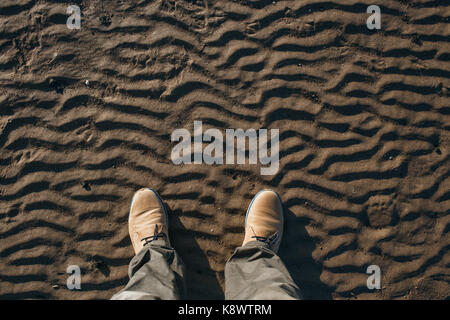 Top view of legs and beige suede boots standing on the beach. Stock Photo