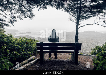 Sad and lonely man sitting on bench overlooking sea on Vancouver Island Stock Photo