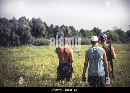 Group of strong male hunters going through rural field with tall grass   during hunting season Stock Photo