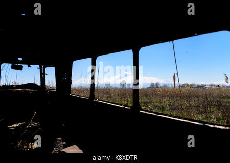 View from inside of an abandoned and rusty old Soviet Russian bus in the middle of reeds and agriculture fields with snow-capped scenic Ararat mountai Stock Photo