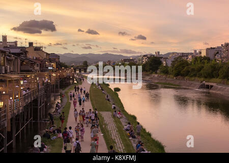 People come together along the Kamo river (Kamogawa) in Kyoto, Japan, with open air restaurants (left) during sunset. Stock Photo