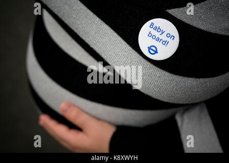 A 9-month pregnant woman holding her bump wears a London Underground Baby on Board badge before boarding the Tube (Editorial use only). Stock Photo