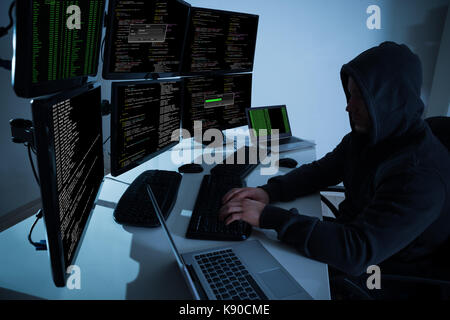 Rear view of hacker using computers to steal data in office Stock Photo