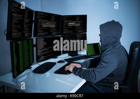 Rear view of hacker using computers to steal data in office Stock Photo