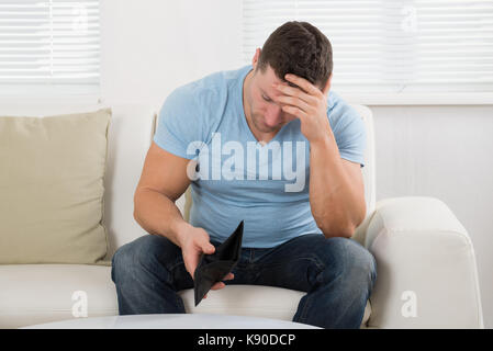 Upset mid adult man holding empty wallet while sitting on sofa at home Stock Photo
