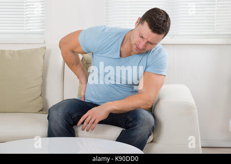 Mid adult man suffering from backpain while sitting on sofa at home Stock Photo