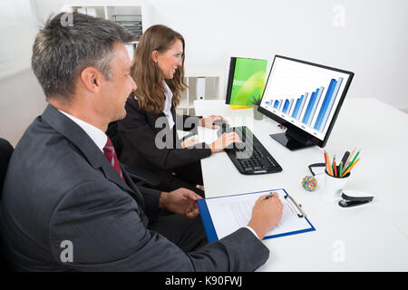 Two Businesspeople Analyzing Graph On Computer In Office Stock Photo
