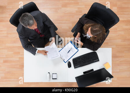 High Angle View Of Two Businesspeople Discussing On Documents In Office Stock Photo