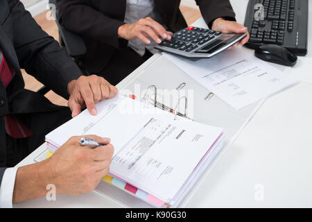 Close-up Of Two Businesspeople Calculating Invoice With Calculator At Desk Stock Photo