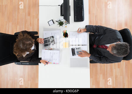 High Angle View Of Two Businesspeople Calculating Bills In Office Stock Photo