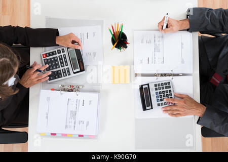 High Angle View Of Two Businesspeople Calculating Bills In Office Stock Photo
