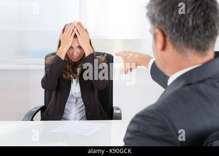 Mature Businessman Pointing To Frustrated Businesswoman In Office Stock Photo