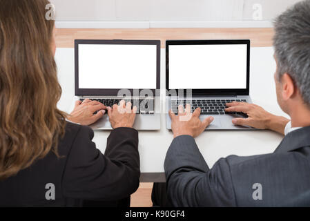Close-up Of Two Colleagues Working On Blank Display Laptop At Desk Stock Photo