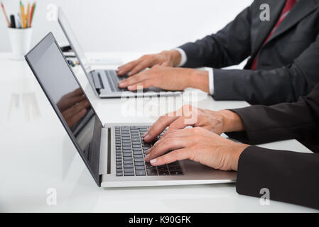 Close-up Of Two Businesspeople Using Laptop At Desk Stock Photo