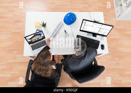 High Angle View Of Two Architects Discussing Blueprint In Office Stock Photo