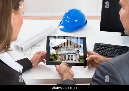 Close-up Of Two Architects Looking At House On Digital Tablet At Desk Stock Photo