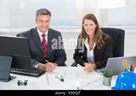 Two Architects Together Discussing Blueprint At Desk In Office Stock Photo