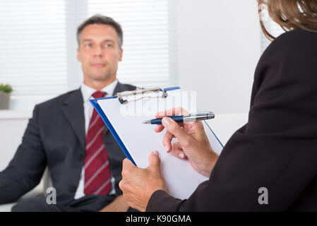 Close-up Of Female Psychiatrist Writing On Clipboard In Front Of Patient Stock Photo