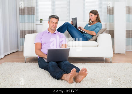 Mature Happy Couple Using Laptops In Living Room Stock Photo