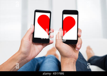 Close-up Of Two People Hands With Mobile Phones Showing Two Halves Of Heart Shape Stock Photo