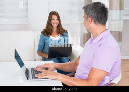 Happy Mature Couple Using Laptops In Living Room Stock Photo