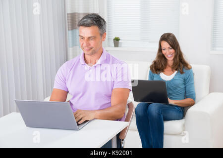 Man Using Laptop In Front Of Woman Sitting On Sofa With Laptop At Home Stock Photo