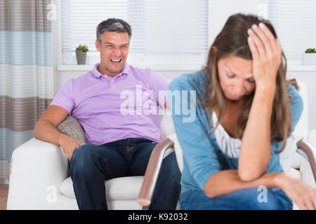 Mature Man Shouting To The Frustrated Woman Sitting On Chair Stock Photo