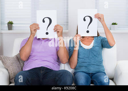 Couple Together Sitting On Sofa Hiding Face With Question Mark Sign Stock Photo