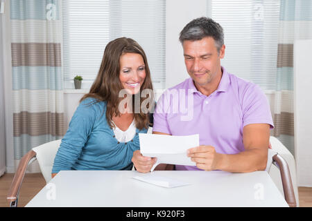 Portrait Of Smiling Couple Sitting In Living Room Reading Letter Together Stock Photo