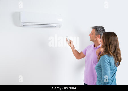 Mature Couple Standing In Front Of Air Conditioner And Adjusting The Temperature By Remote Stock Photo